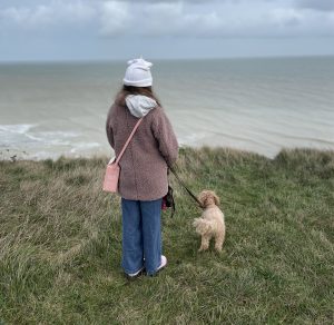 A little girl in a fluffy pink coats and her cavapoo puppy stand on the cliffs in Deal Kent taken by the house in deal