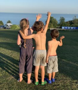 3 children with their backs to the camera, wave to someone in the distance. The image conjures up summertime fun on holiday. Shot taken by The House in Deal holiday cottage