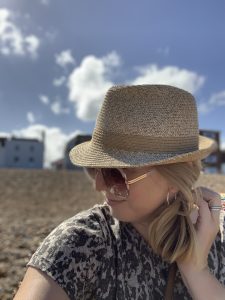 picture of the host of the house in deal sitting on deal beach and wearing a hat and shades. her face is partially obscured the these as she turns to the side
