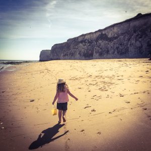 Picture of a little girl walking along a beach with cliffs in the background, shot taken by The House in Deal, a holiday cottage to rent in Deal kent