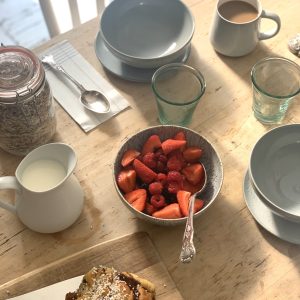 a table set for breakfast with a bowl of strawberries.